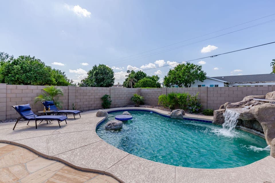 Stunning backyard retreat featuring a private pool with a waterfall, sun loungers, BBQ grill, outdoor seating, Smart TV, and an outdoor dining area.