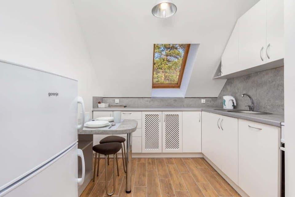 A kitchen with a dining area, a white countertop, and a wooden table with two chairs, seamlessly connected to a cozy lounge corner.
