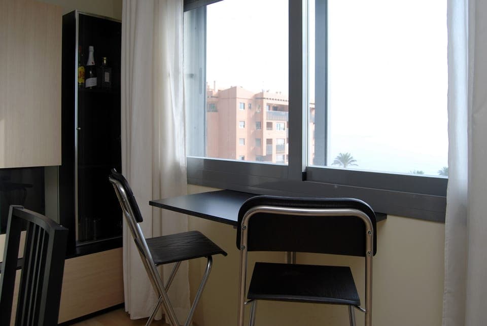 Breakfast or work nook maximizing natural light and exterior views. Compact arrangement with a fold-down table and folding chairs, ideal for optimizing small spaces.