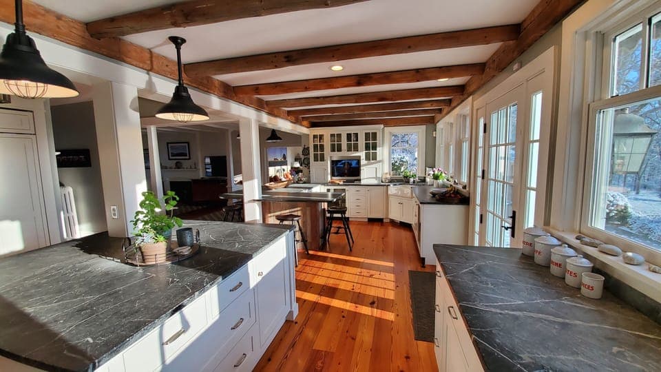 View across kitchen from center island to 7 stool counter, TV and bar area.