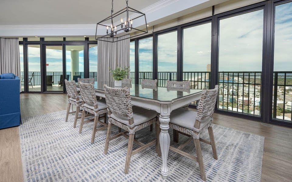 This dining area features a stylish table with eight woven chairs, with expansive windows offering a stunning beach view
