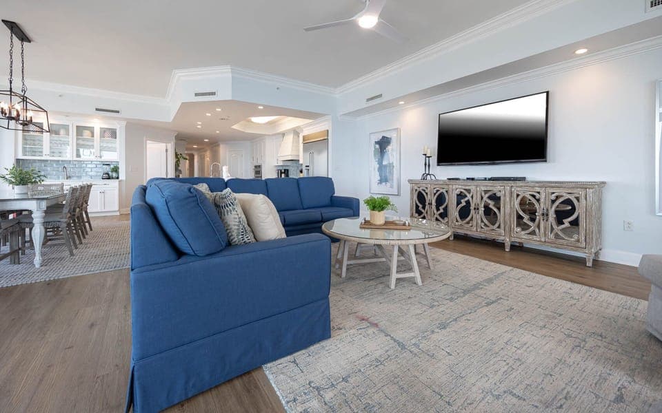 The bright living area features a blue sofa, a stylish coffee table, and a large TV, perfect for relaxing after a beach day
