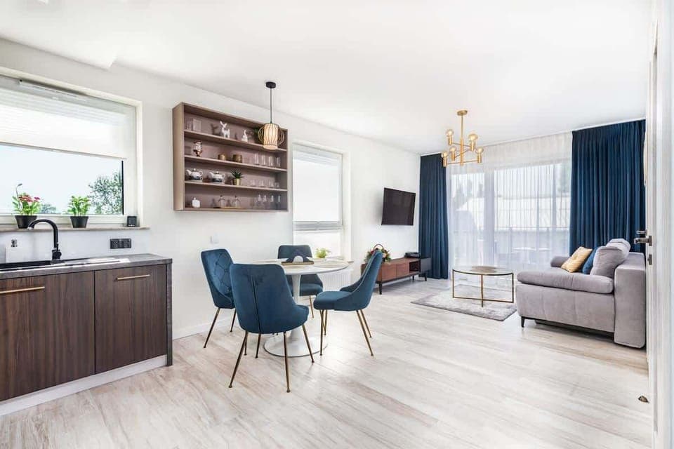  A modern living room with light-colored flooring, a stylish table, dark blue curtains, and comfortable furniture. The room features a cozy and elegant design.