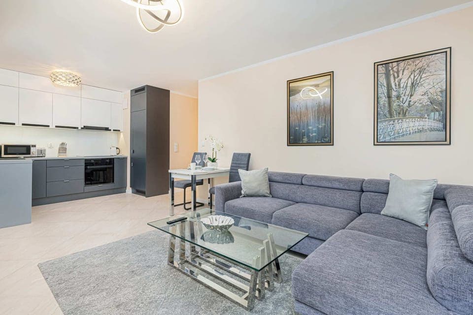 A bright and comfortable living room featuring a stylish gray sofa, a glass coffee table, and elegant wall art.