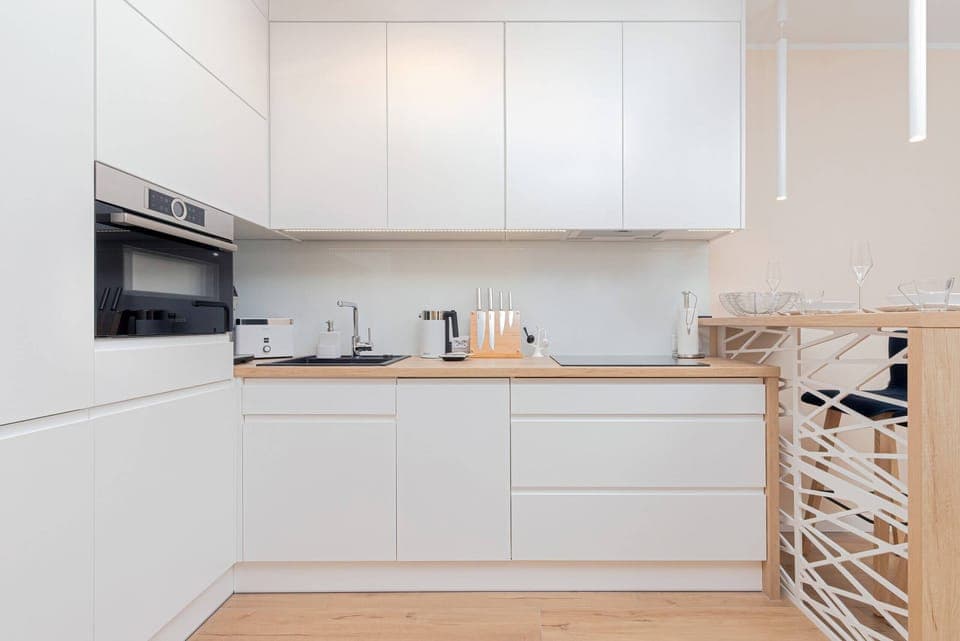 A sleek, white kitchen with minimalist cabinetry and a cozy dining area featuring light wood accents and subtle decorative touches.