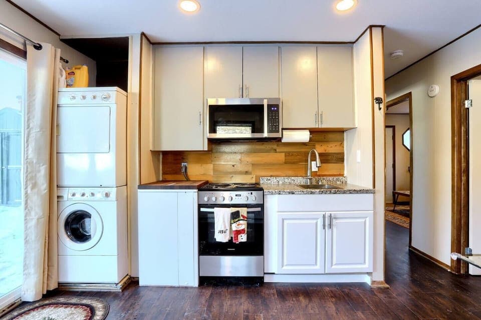 - Make meals with ease in a fully equipped kitchen featuring granite countertops & gas stove
- Enjoy added convenience with in unit laundry tucked neatly beside the cooking area
- Wood backsplash and soft lighting create a warm, modern cabin vibe