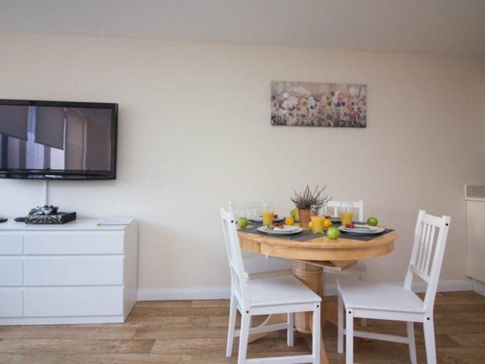Round dining table set for four, chest of drawers, mounted TV, and wall art in neutral apartment – Castle 6 - Southampton