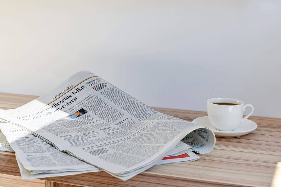 A small desk with a coffee cup and a newspaper, perfect for a peaceful morning. The surface is wooden, complementing the simple decor.