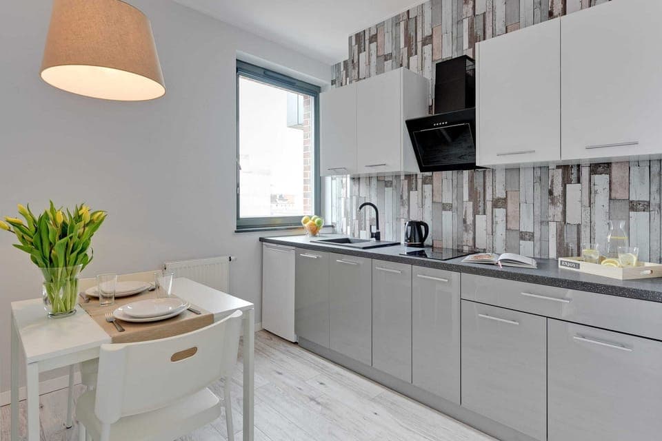 A compact kitchen with sleek gray cabinets and a decorative backsplash. A vase with flowers adds a welcoming touch to the minimalist design.