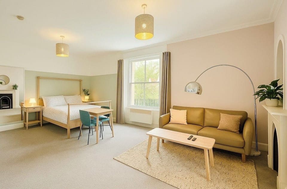 Bright and spacious open-plan suite with a cozy seating area, modern lighting, and leafy accents. Relax and recharge in the inviting bed and chic neutral decor. The perfect spot for a peaceful and stylish getaway.