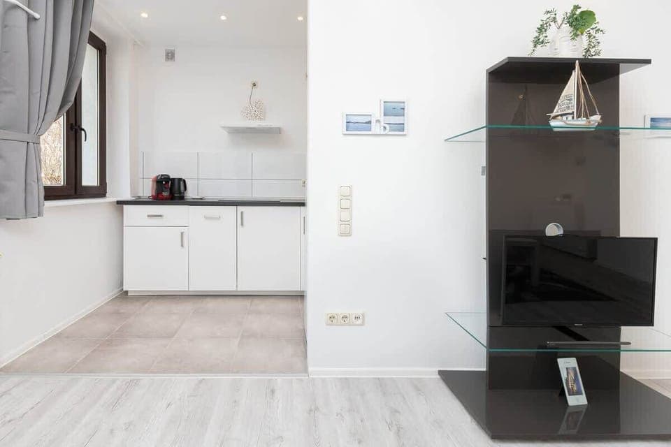 View from the living area with black bookcase to the kitchenette with white furniture.