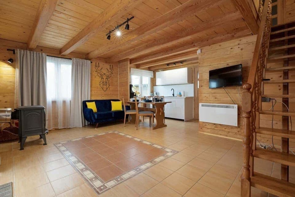  A cozy living room with wooden interiors, a comfortable sofa, a dining area, and large windows letting in natural light, creating a warm and inviting space.