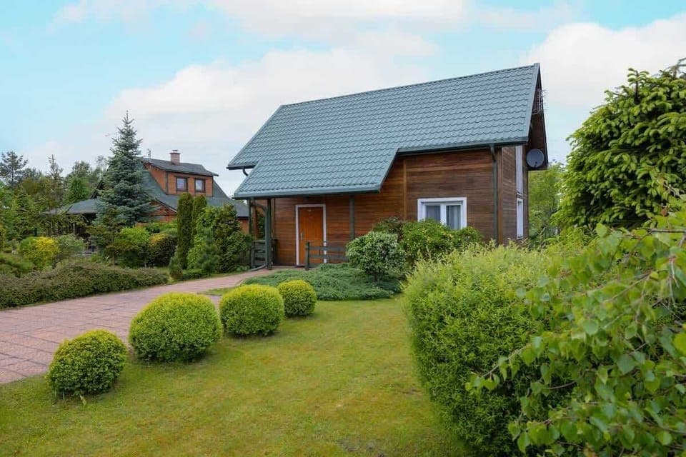 A charming wooden cabin surrounded by lush greenery and a well-maintained lawn, creating a serene countryside atmosphere.
