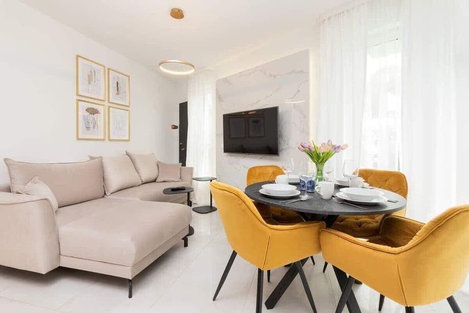 Bright living room with beige sofa, TV, and dining table with yellow chairs.