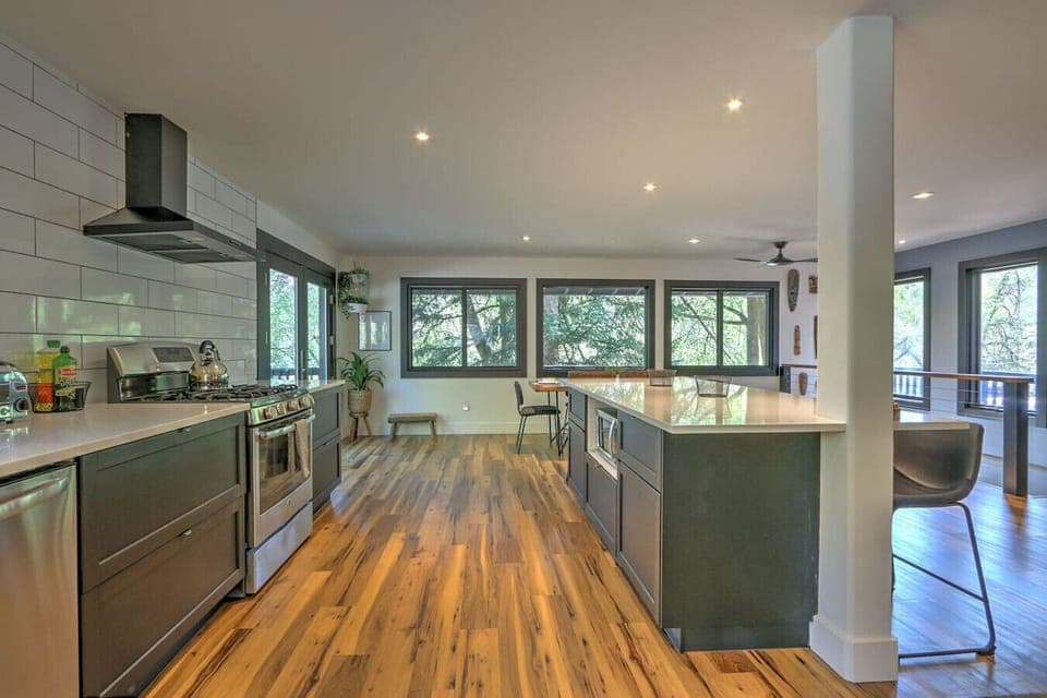 Open concept chef`s kitchen with large windows overlooking trees & deck