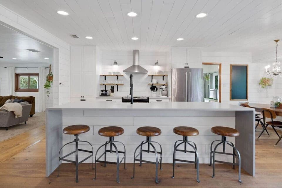Bright farmhouse kitchen with open shelving and river‑view dining table—cook together, then step right out to the treetop deck.