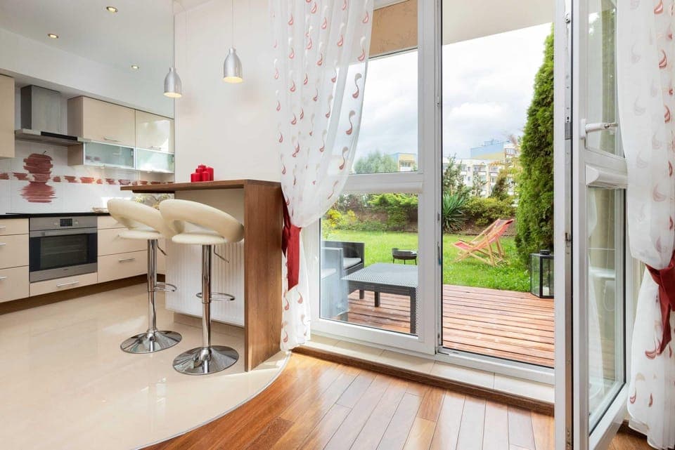 A modern kitchen with light wooden cabinets, a view of a patio area with green grass, and plenty of natural light.