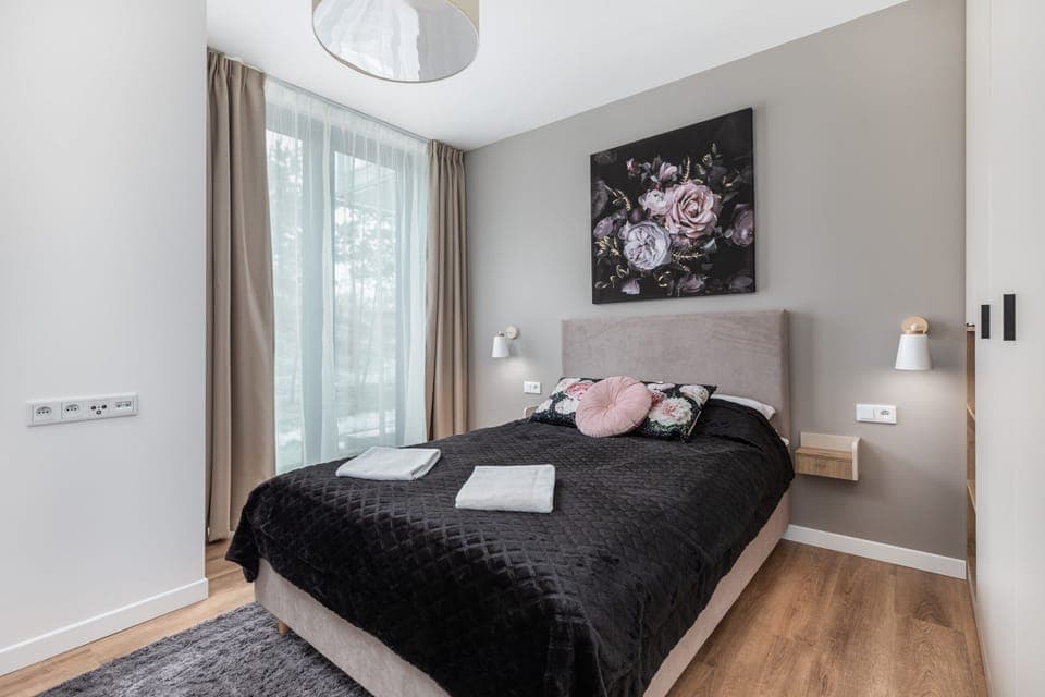 Modern bedroom with double bed with black bedspread. On the wall hangs a painting depicting flowers on a black background.