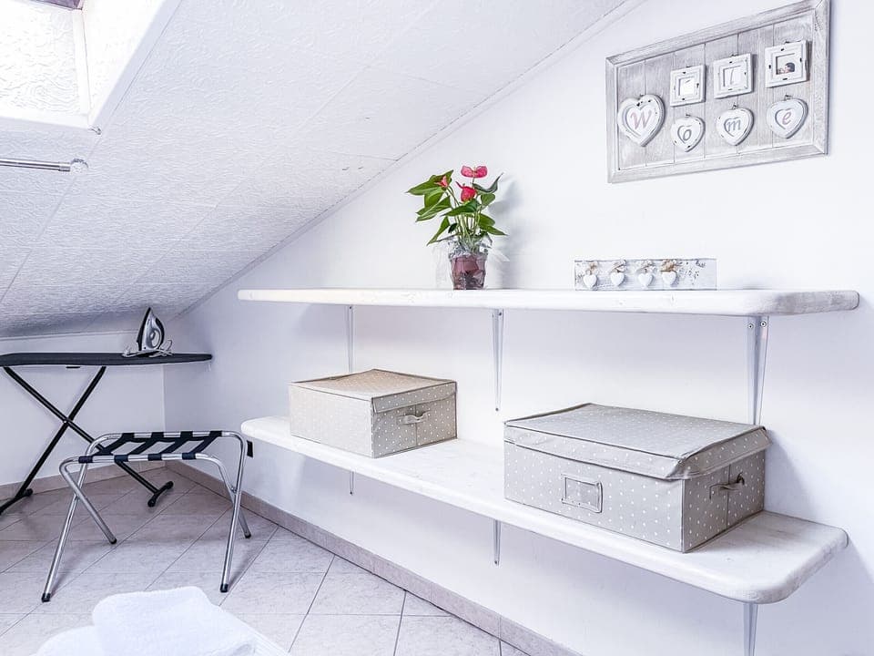 Double bedroom with iron and ironing board, suitcase rack, and practical shelves with clothes boxes for optimal organization of the space