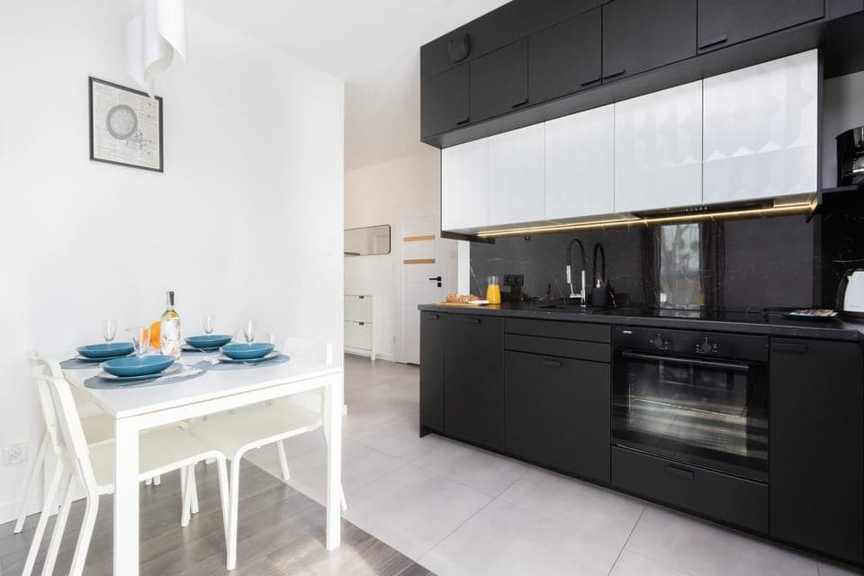A sleek, modern kitchen with black and white cabinets, an adjoining dining area with a set table for two.