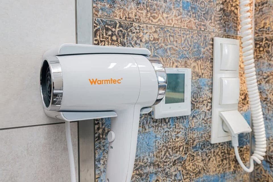 A wall-mounted hairdryer placed conveniently in the bathroom, alongside a sleek, modern backsplash for a functional and stylish look.