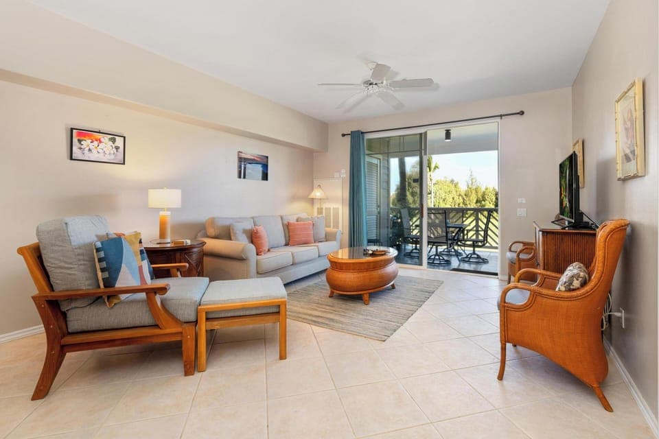 - Bright living room with plush sofa, armchairs, and coffee table set on tiled floors   - Sliding glass doors open to a balcony with scenic views and fresh breezes   - Neutral tones and ceiling fan create a comfortable, airy gathering space