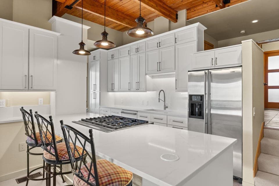 Your gourmet kitchen awaits with gleaming white cabinetry, expansive quartz countertops, and rustic wooden beam ceilings that create the perfect blend of elegance and warmth for your culinary adventures.