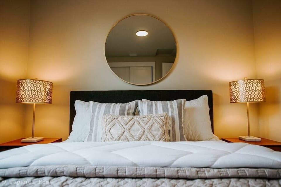 Golden circular mirror over the cozy bed frame brings a classy accent to the room