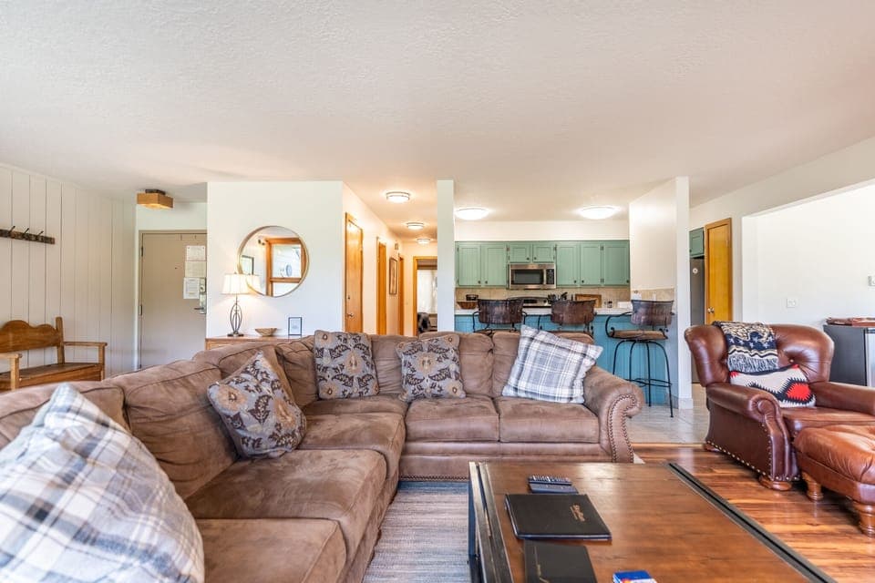Spacious living area with large mounted flat screen TV, hardwood flooring, access to the private balcony, wood burning fireplace and ample seating.