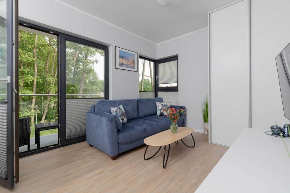 A modern living room features a cozy gray sofa, a black coffee table, and large floor-to-ceiling windows allowing ample natural light.