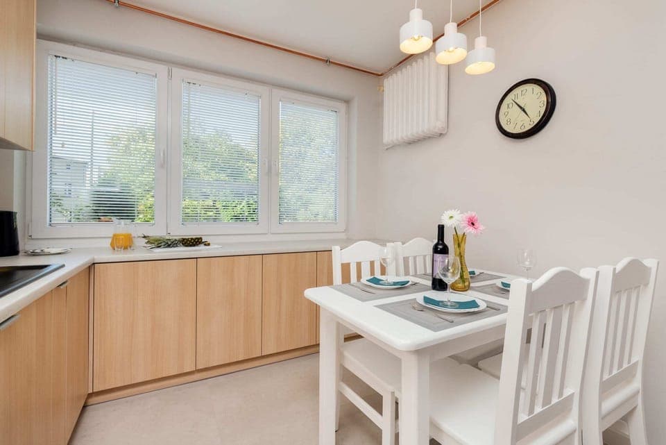 A dining area and kitchen featuring wooden cabinets, a white dining set, and large windows for plenty of natural light.
