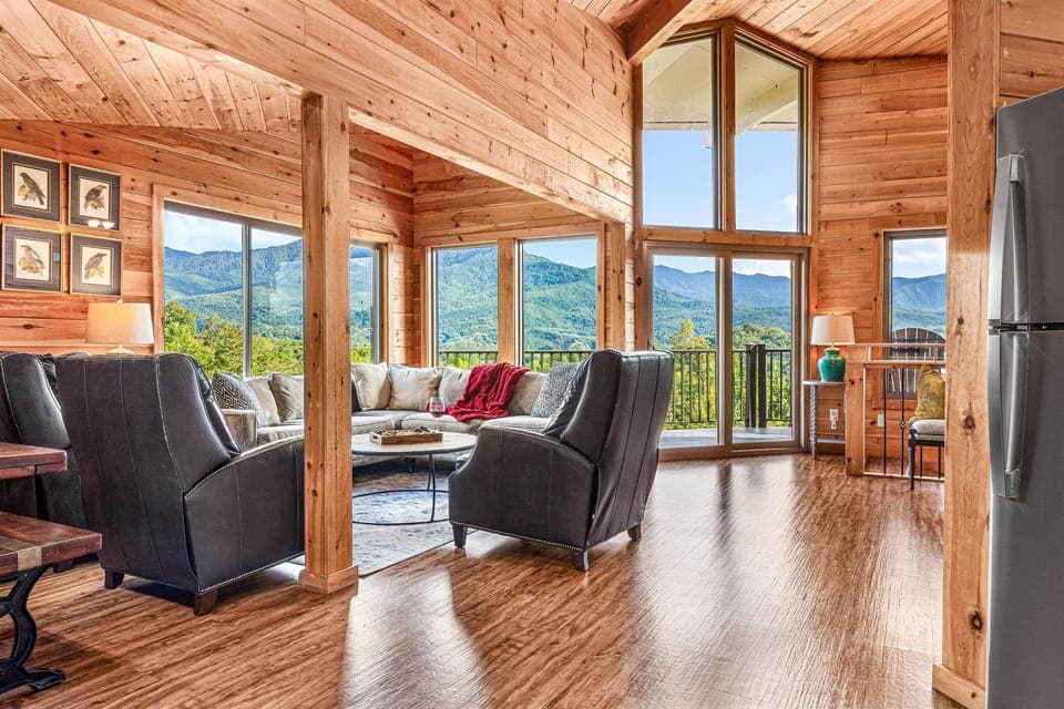 The open-plan living area on the upper level is anchored by a wall of windows and soaring vaulted ceilings. Comfortable seating, warm wood tones, and that view —always the view. Step through the door and onto the balcony with the Smokies spread before you.