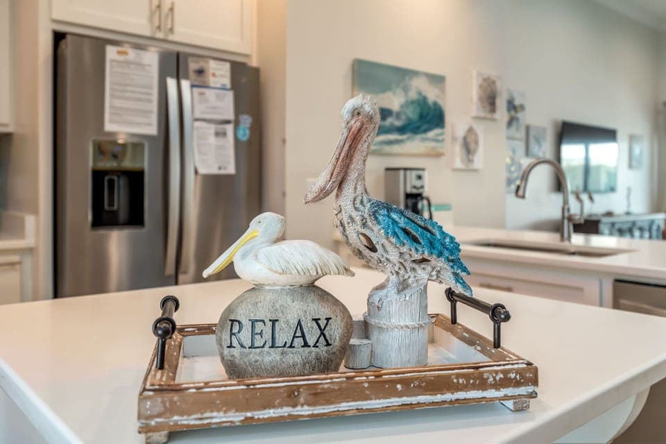 Your coastal kitchen invites relaxation with elegant white cabinetry, modern appliances, and charming beach-themed touches that capture seaside serenity.