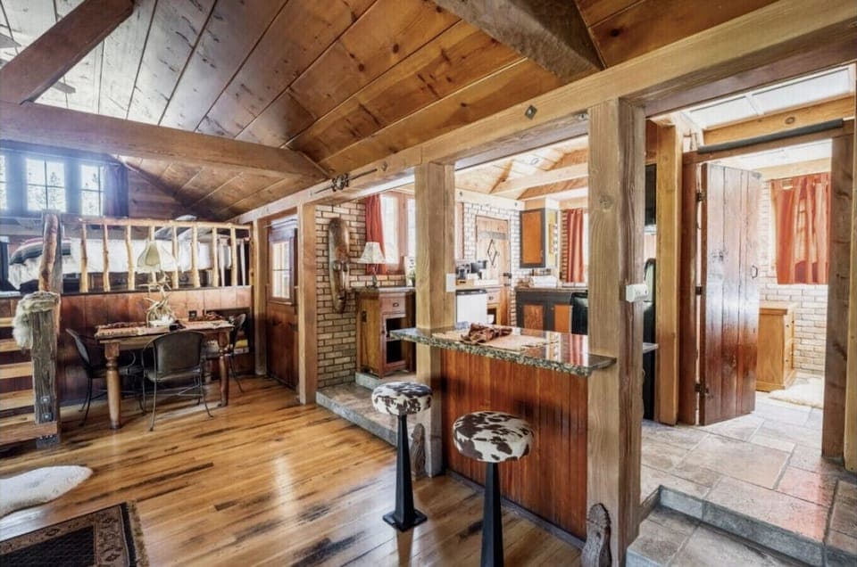 Charming rustic cabin interior featuring cozy wooden beams, a welcoming breakfast bar with patterned stools, and a warm dining nook perfect for gathering and making memories.