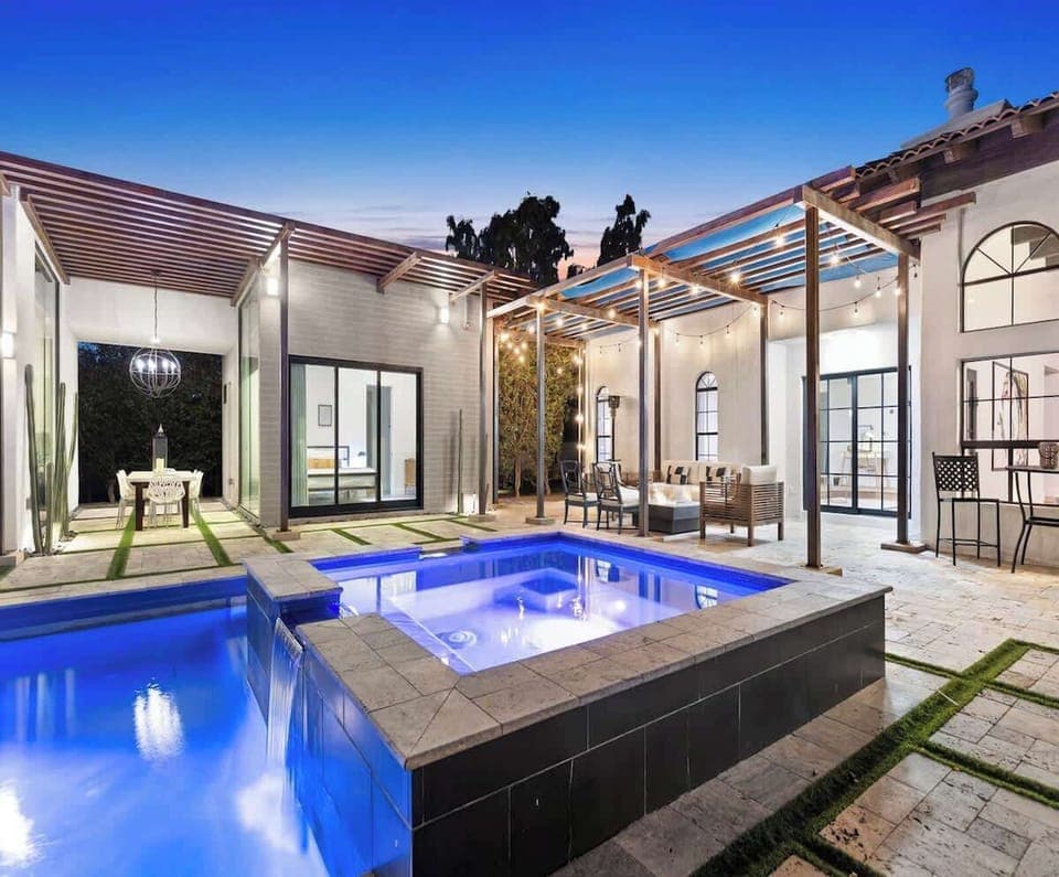 Modern outdoor patio with a lit pool and covered seating area for relaxing evenings.