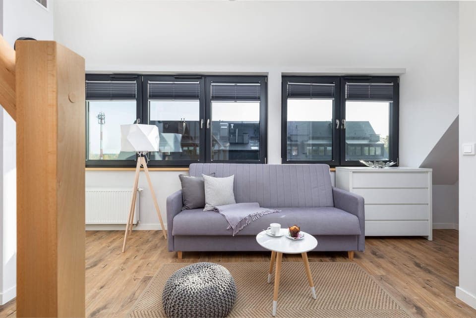 A bright living room with a modern sofa, coffee table, and a view of large windows.
