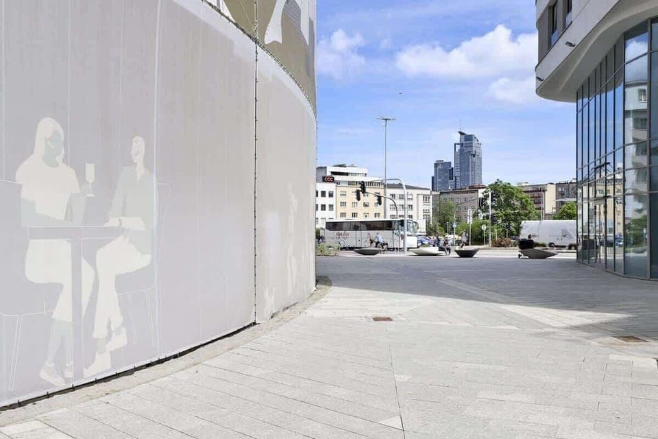 Urban walkway with modern architecture, curved walls, and a view of the city skyline.
