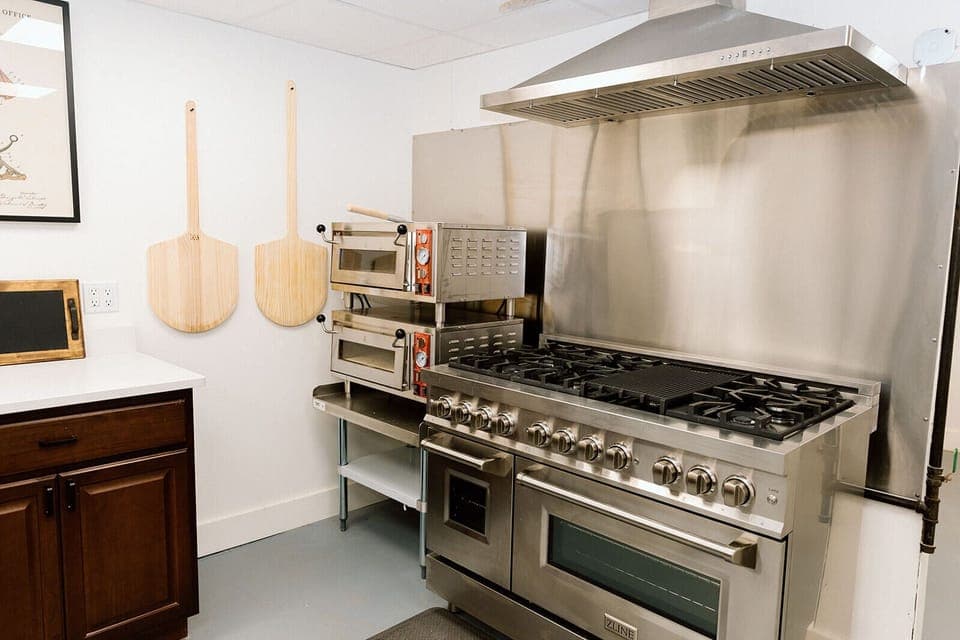 Commercial kitchen with pizza ovens, dual ovens, and prep space.