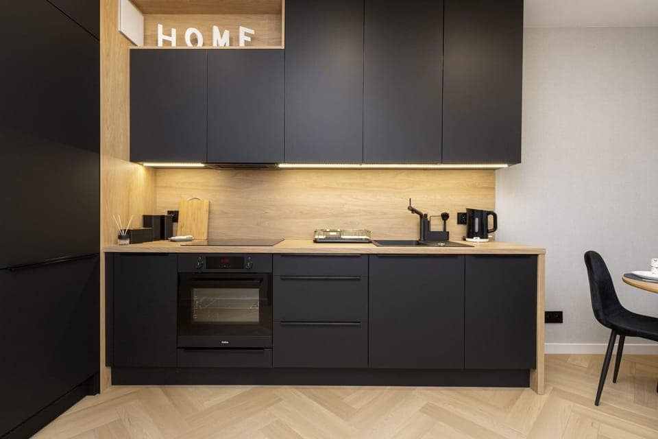A compact kitchen with dark blue cabinets, under-cabinet lighting, and a small dining table in the background.