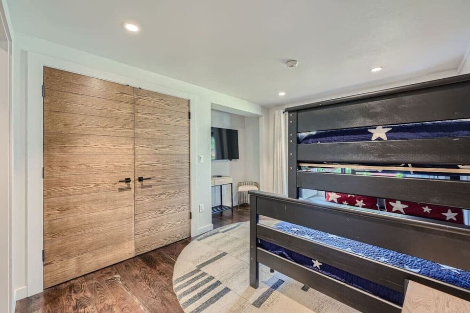 The Downstairs Bunk Room features cozy bunk beds and stylish decor, sharing a luxurious bathroom with the Middle Queen Bedroom, which has a steam shower and double vanity. Both rooms enjoy access to a shared patio, perfect relaxation & quality time