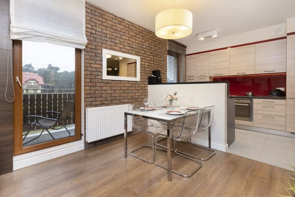 The dining area features a modern table with chairs and a large mirror on the wall, creating a sense of depth in the room. The kitchen is visible in the background, blending seamlessly with the dining space.