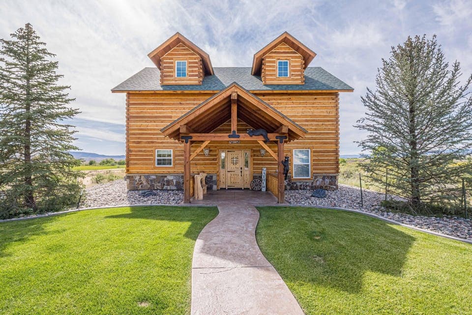 Front exterior of the log cabin-style house with a covered porch, stone foundation, and manicured green lawn.