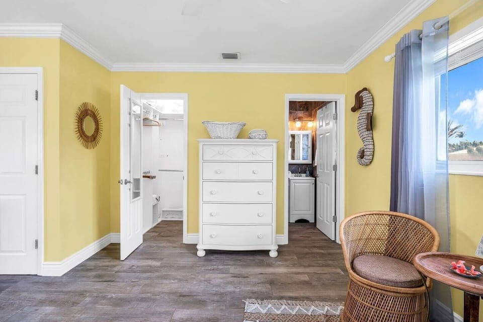 Tropical-style master bedroom with sunny yellow tones, a pull-out sofa, large smart tv, and an en-suite bathroom.