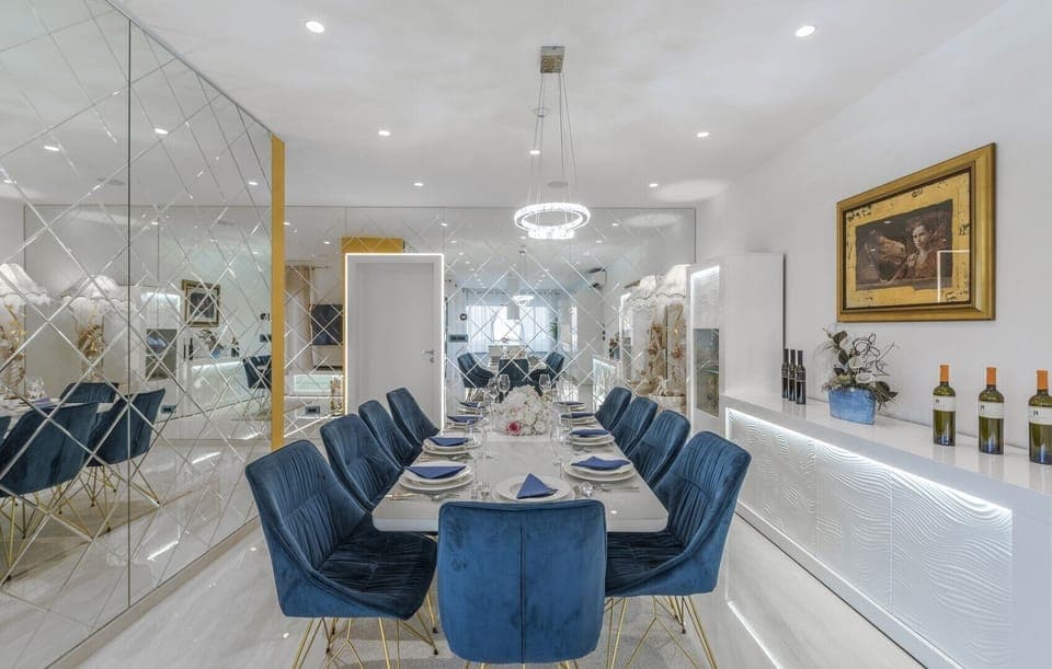 A set dining table with blue velvet chairs for 10 people and an illuminated wine bar next to the table in the dining area of the kitchen.