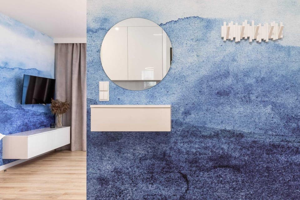 A bedroom with a modern design, featuring a round mirror, blue accents, and a stylish wall feature.
