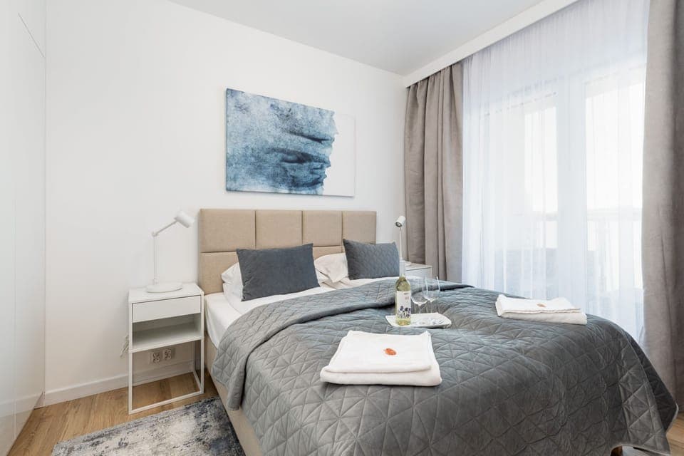 A cozy bedroom with a neatly made bed, soft gray bedding, and modern bedside tables.
