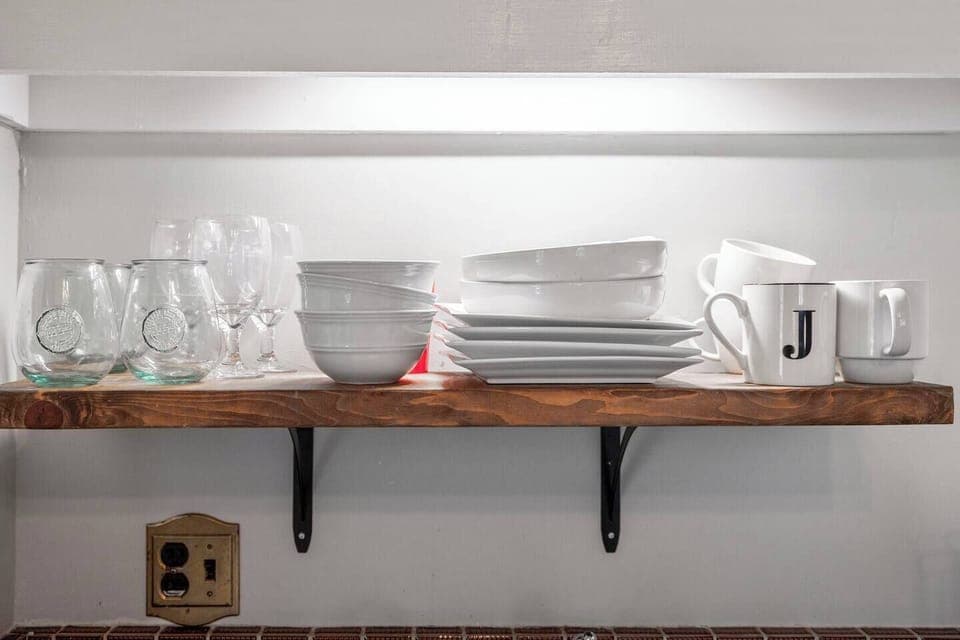 Plates and cups on shelf above kitchen sink.