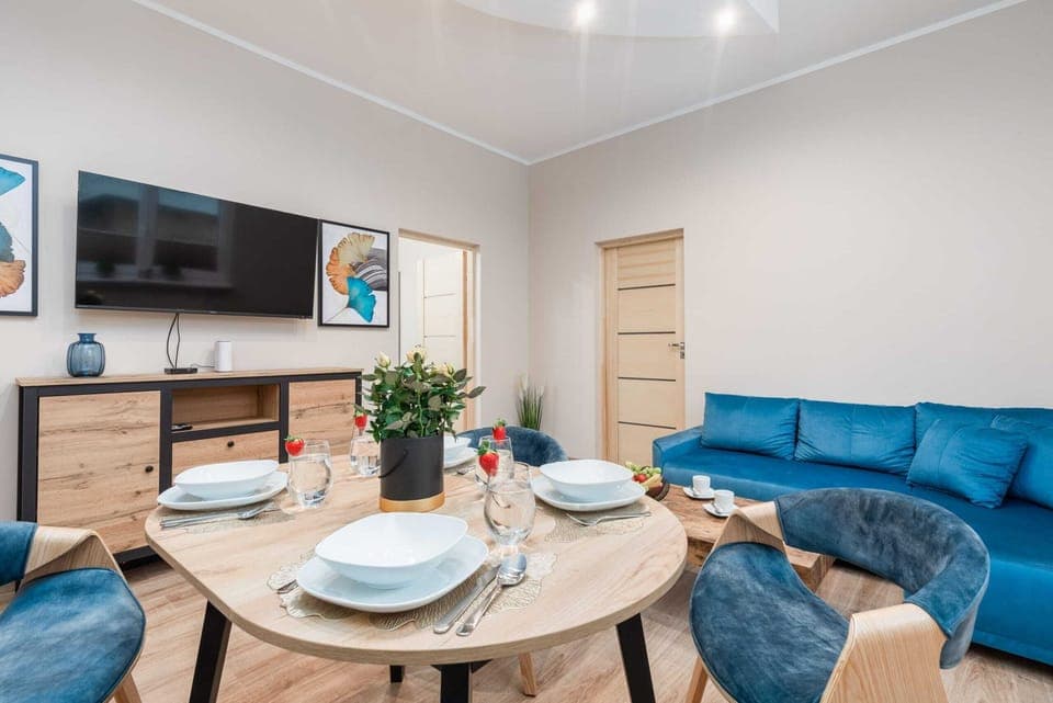 A cozy living room with a blue sofa, round coffee table, and a wall-mounted TV.

