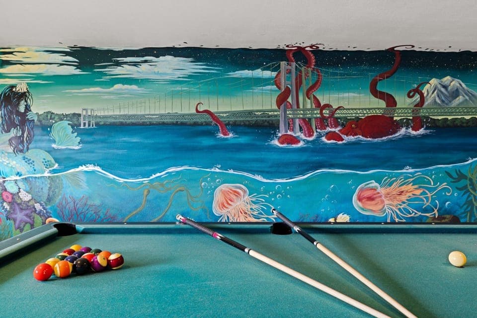 This local artist's hand painted vibrant wall mural transforms this game room space into a masterpiece. Featuring the Narrows Bridge along with iconic Pacific Northwest (PNW) sea life such as the Great Pacific Octopus that she painted as larger-than-life and entwined with the bridge along with a mythical mermaid.