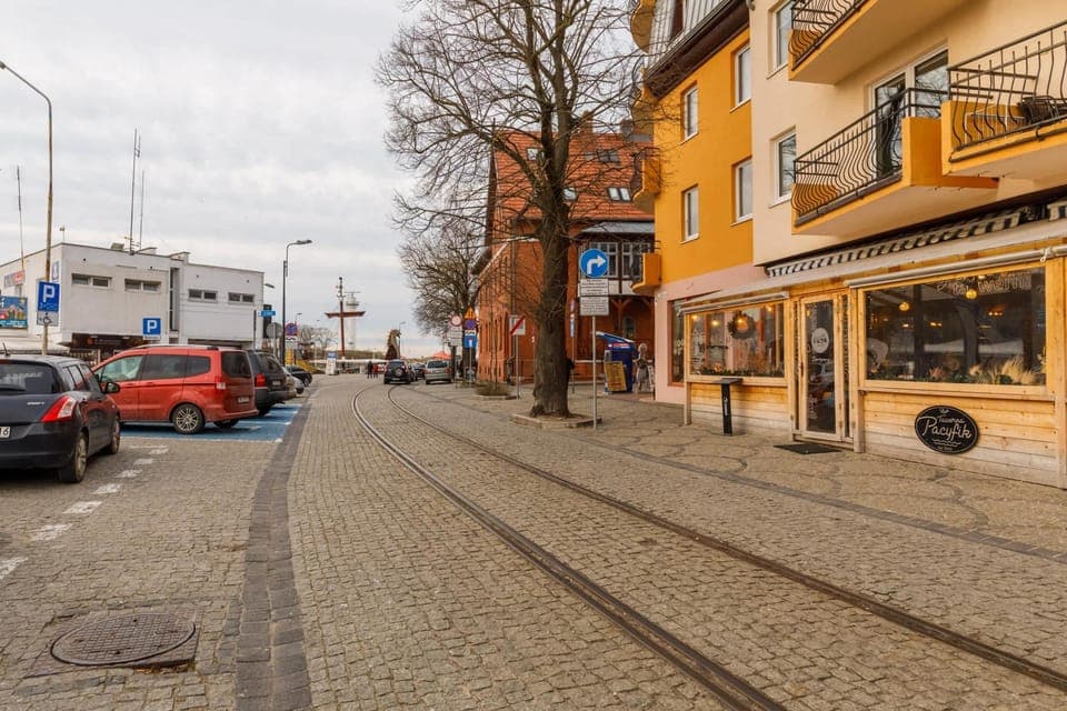 A vibrant street view with cobblestone pavement, shops, and parked cars.
